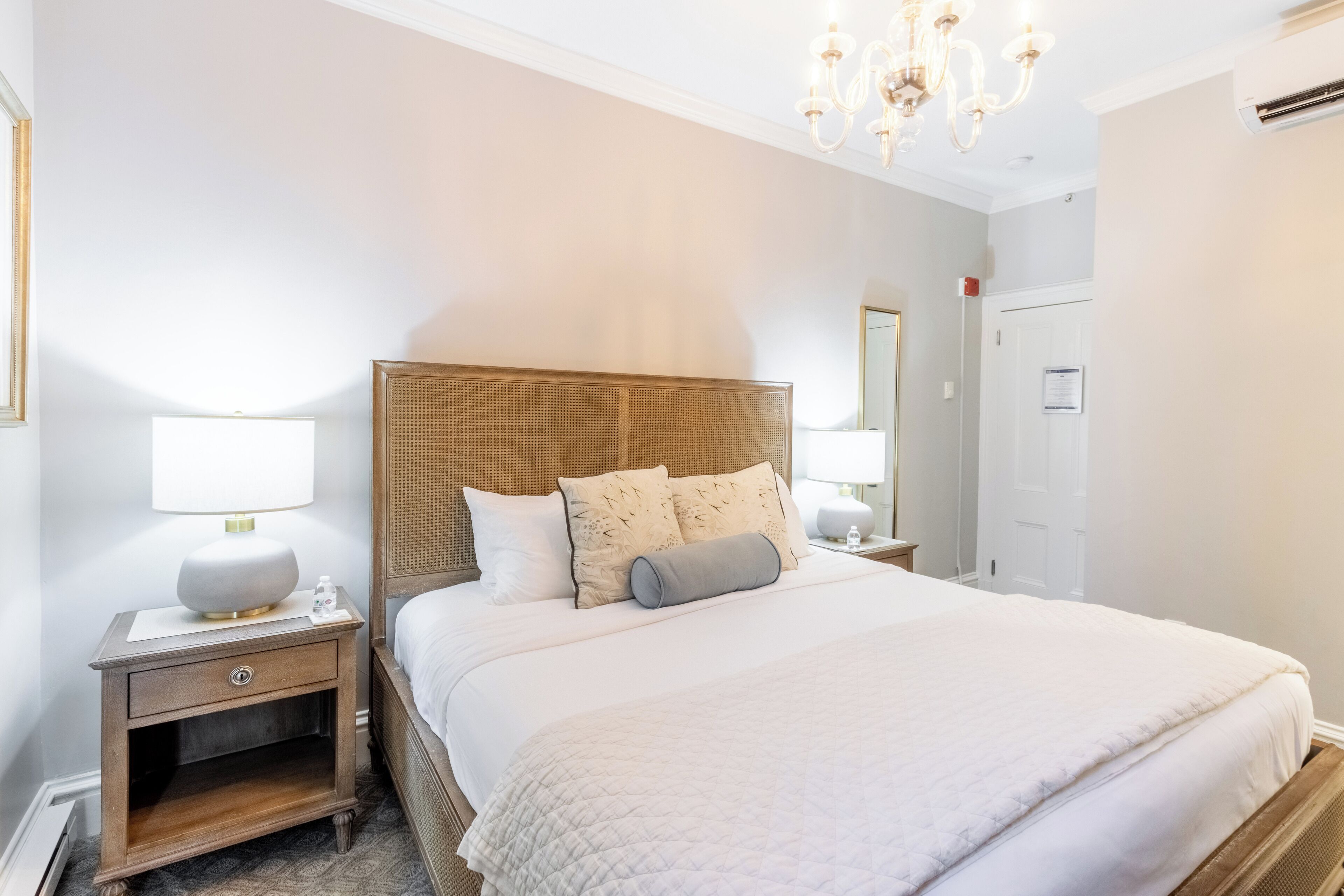 Une chambre à coucher bien aménagée, avec un grand lit, deux tables de chevet, un lustre et une porte.