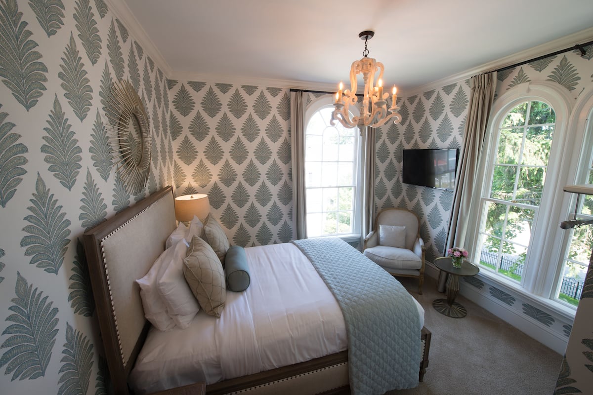 A bedroom with a bed, a chair, a TV, and a window with a view.