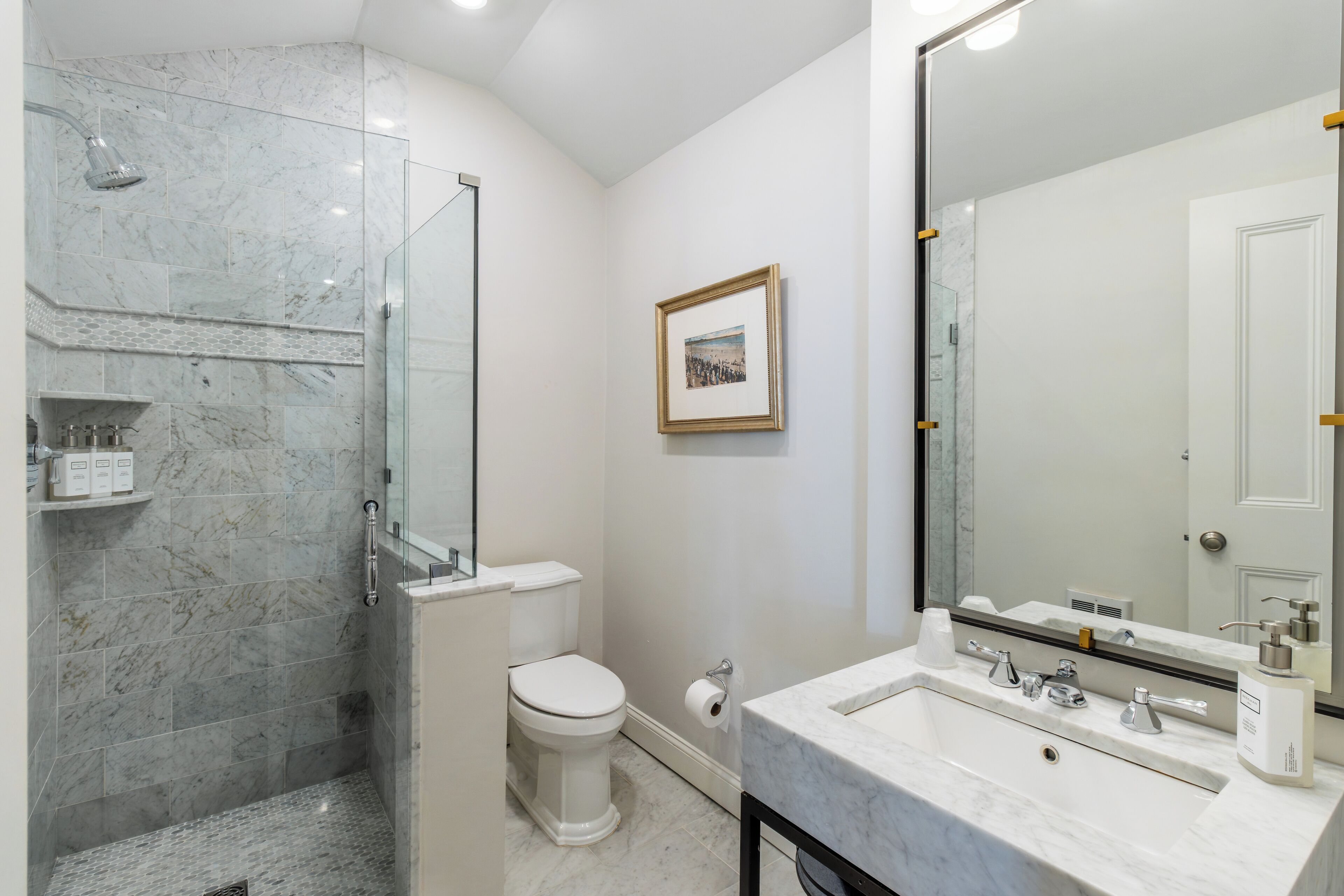 Une salle de bain moderne avec une douche à parois de verre, des toilettes et un grand miroir au-dessus d’un lavabo en marbre.