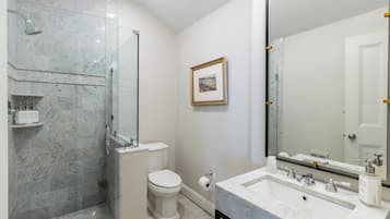 Une salle de bain moderne avec une douche à parois de verre, des toilettes et un grand miroir au-dessus d’un lavabo en marbre.
