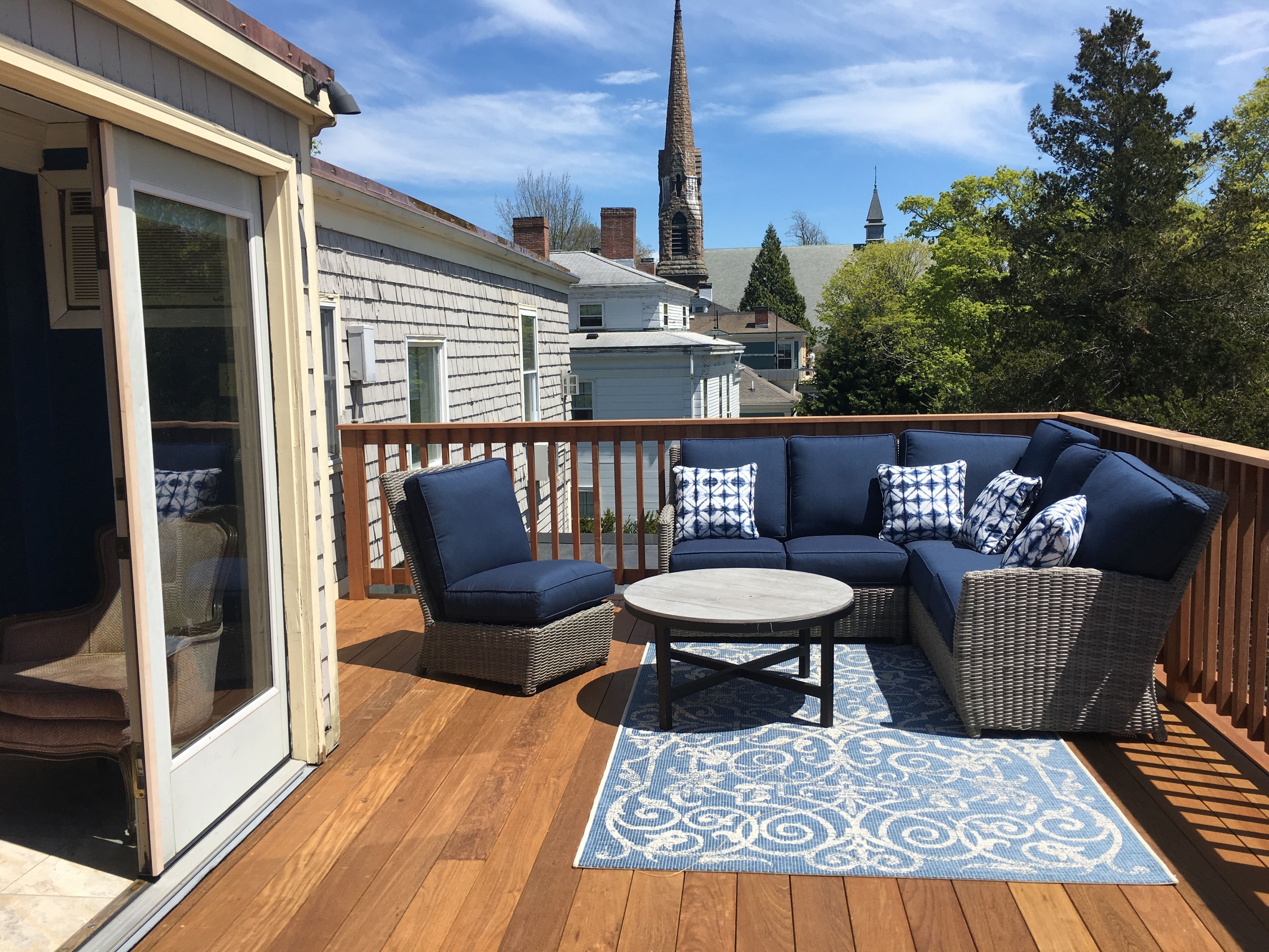 A deck with a wicker sofa, a round table, and a patterned rug.