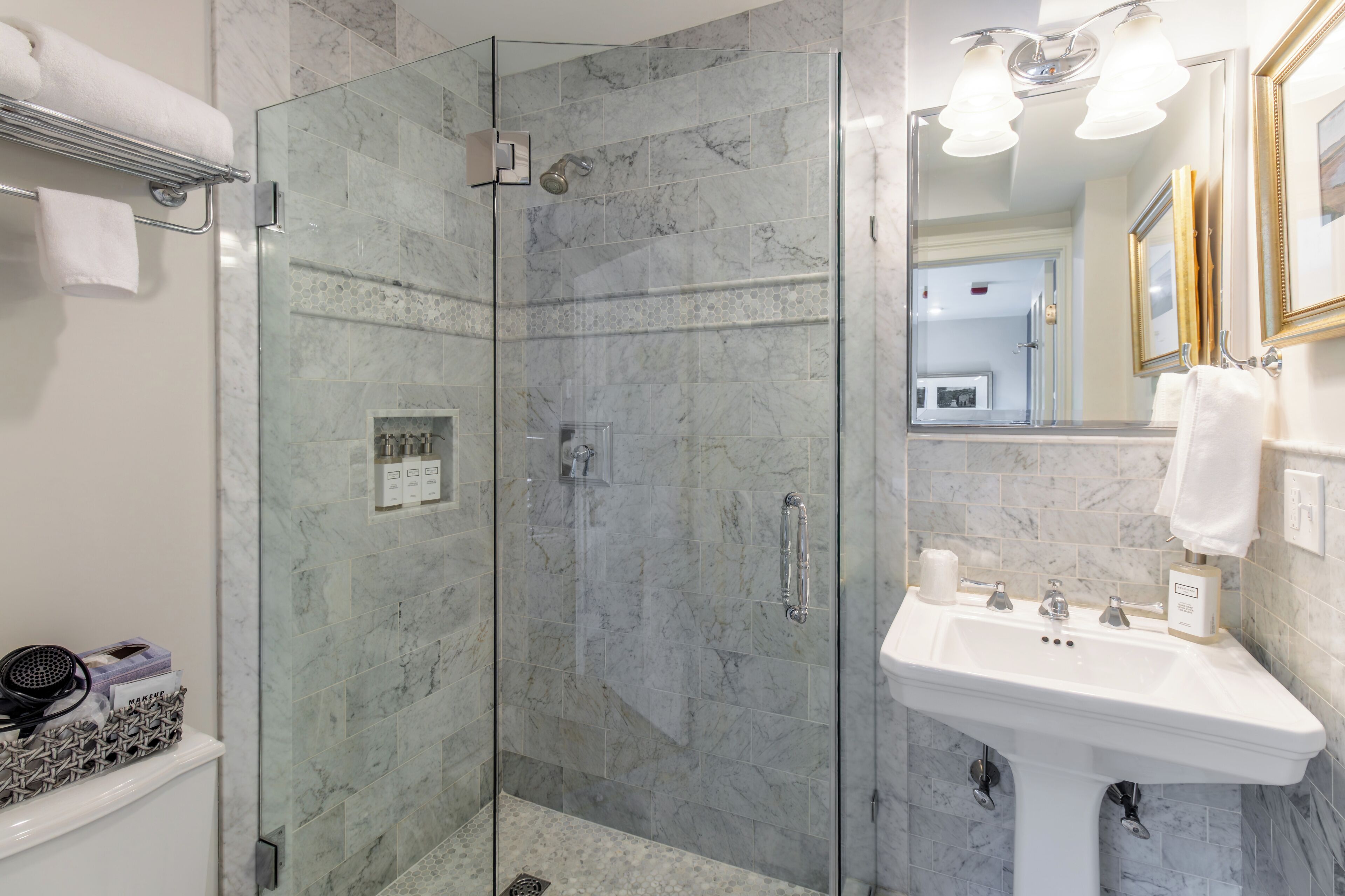 Un baño moderno con ducha de vidrio, lavamanos blanco y pared revestida de mármol.