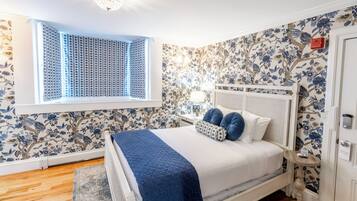 Een slaapkamer met een bed, een raam met zonwering, een muur met bloemenbehang en een plafondlamp.