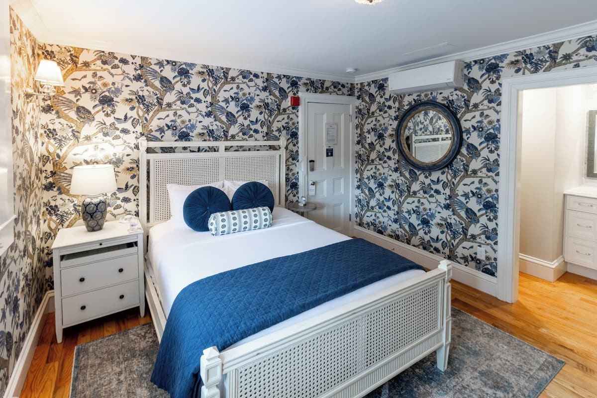 A bedroom with a bed, nightstands, a dresser, a mirror, and floral wallpaper.