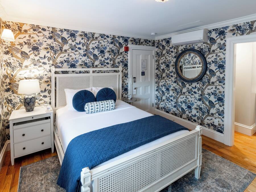 Un dormitorio con cama, mesitas de noche, cómoda, espejo y papel tapiz floral.