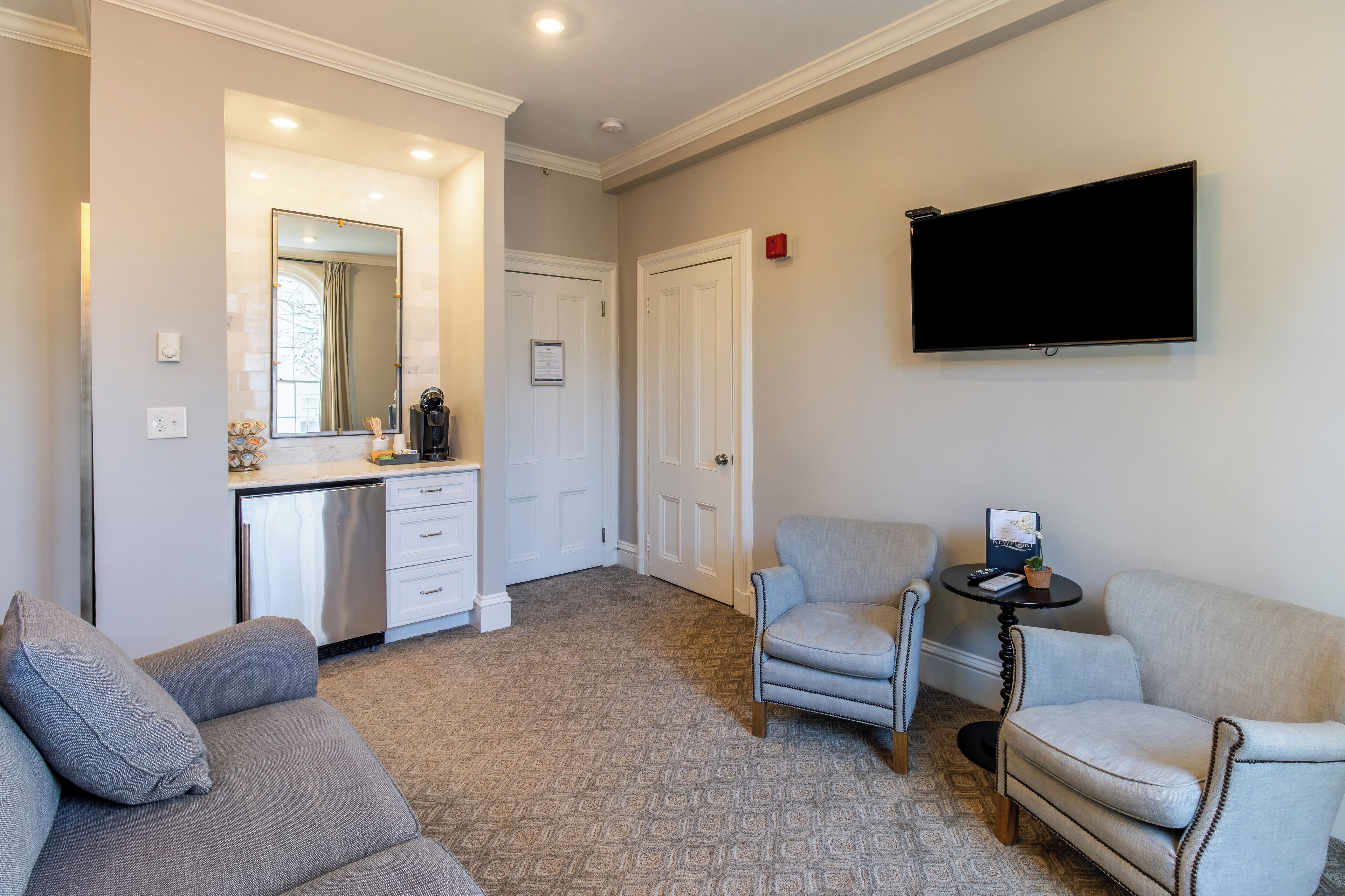 Un salon avec un canapé gris, deux fauteuils, une table basse et un téléviseur à écran plat fixé au mur.