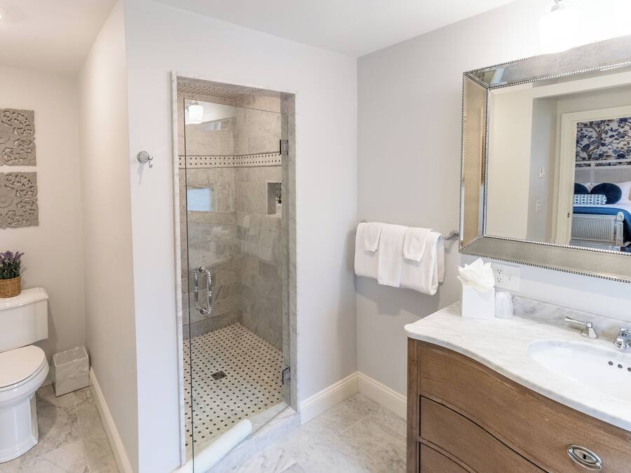 Un bagno moderno con doccia vetrata, un water bianco, un lavabo in marmo e uno specchio grande.