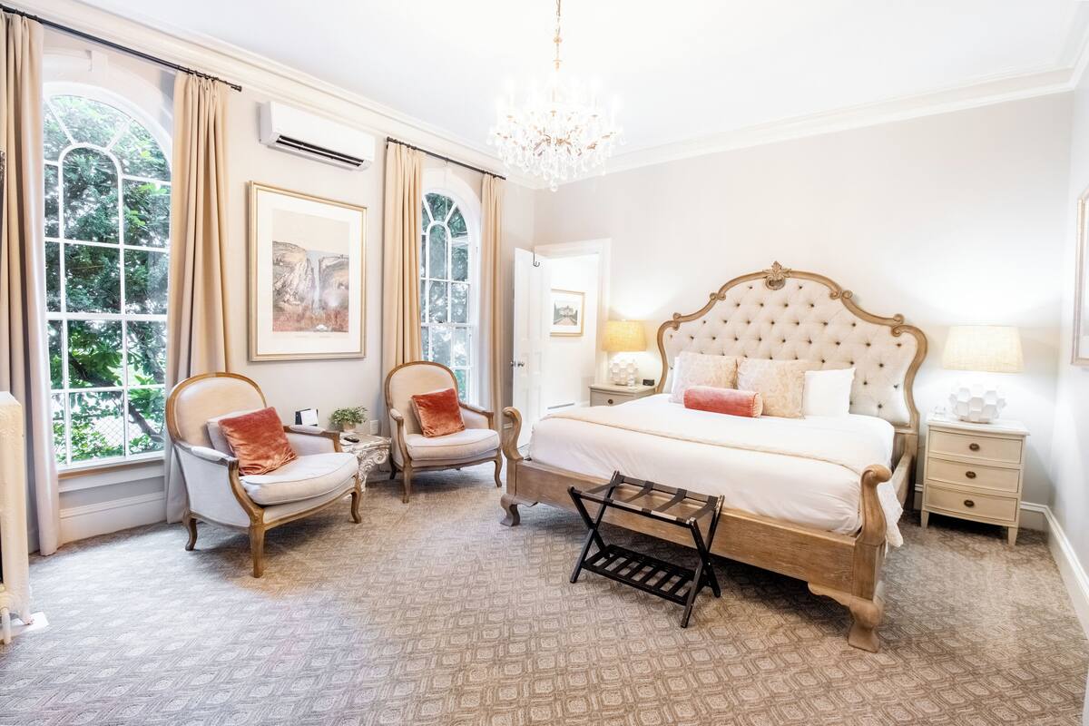 A bedroom with a large bed, two armchairs, a small table, and a chandelier.