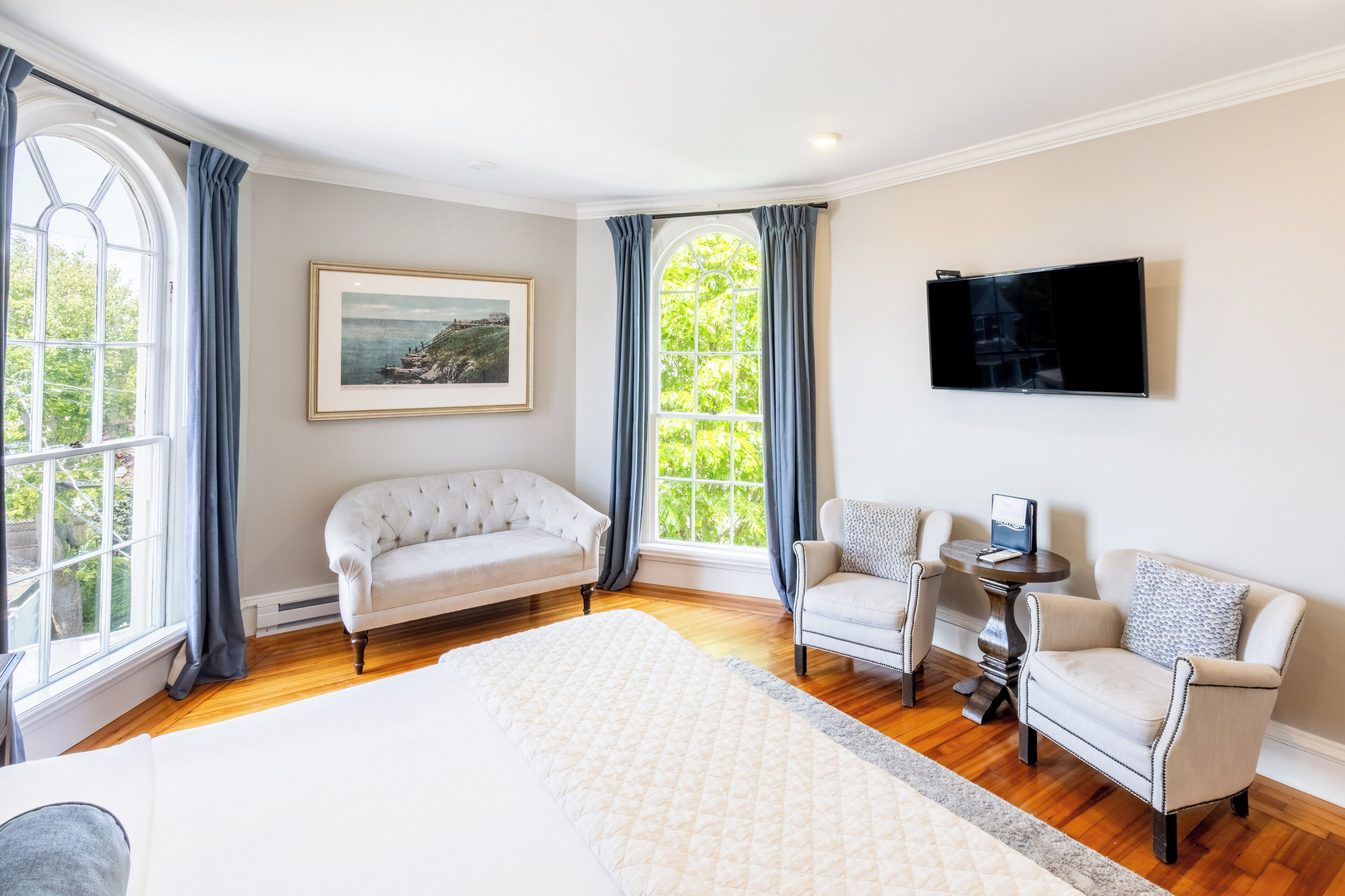 Habitación de hotel con una cama grande, dos sillones, una mesita, un televisor y un cuadro en la pared.