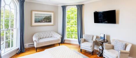 Habitación de hotel con una cama grande, dos sillones, una mesita, un televisor y un cuadro en la pared.