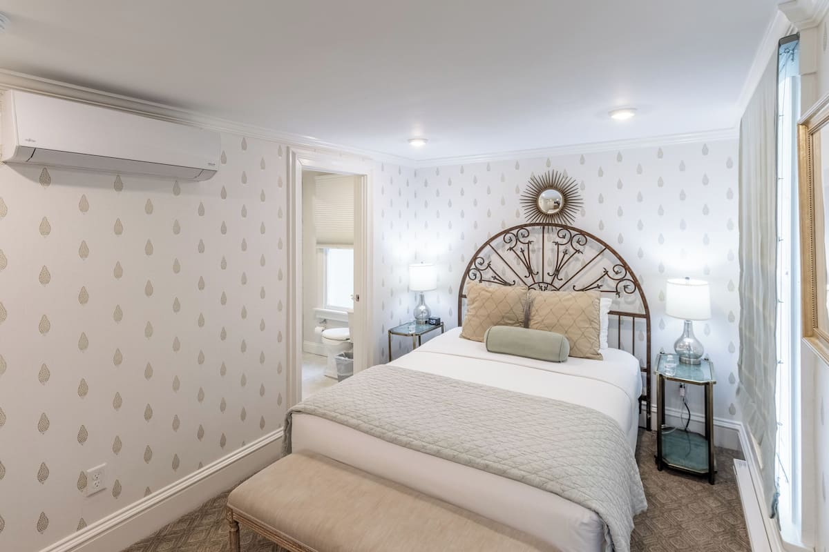 A bedroom with a bed, bedside tables, a nightstand, a mirror, and a window.