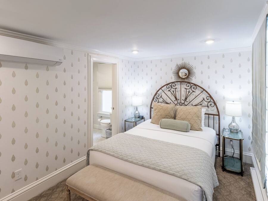 A bedroom with a bed, bedside tables, a nightstand, a mirror, and a window.