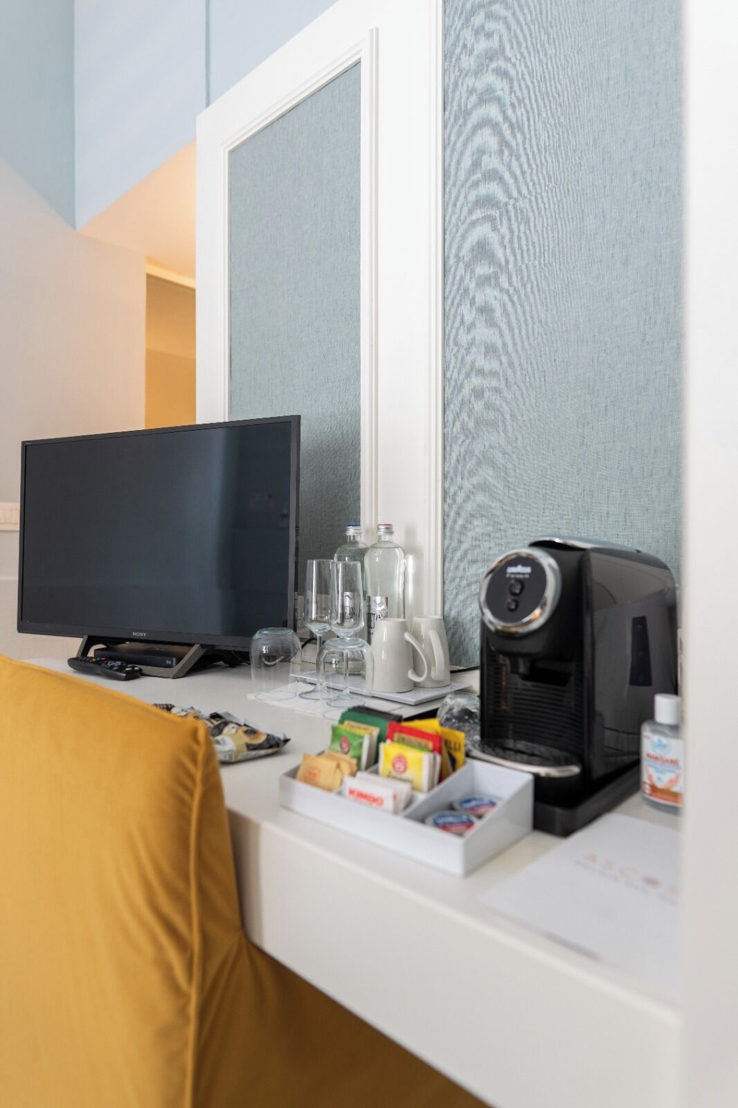 A hotel room with a flat-screen TV, a coffee maker, a glass of water, and a box of tissues on the desk.