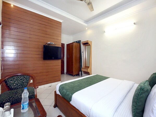 Habitación de hotel con pared de madera, una cama con ropa de cama verde, un televisor montado en la pared y un armario.