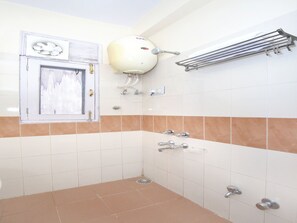 A bathroom with white and beige tiles, a shower with a handheld showerhead, a towel rack, and a window with a decorative element. - OYO 990 Hotel Paradise (Chandigarh)