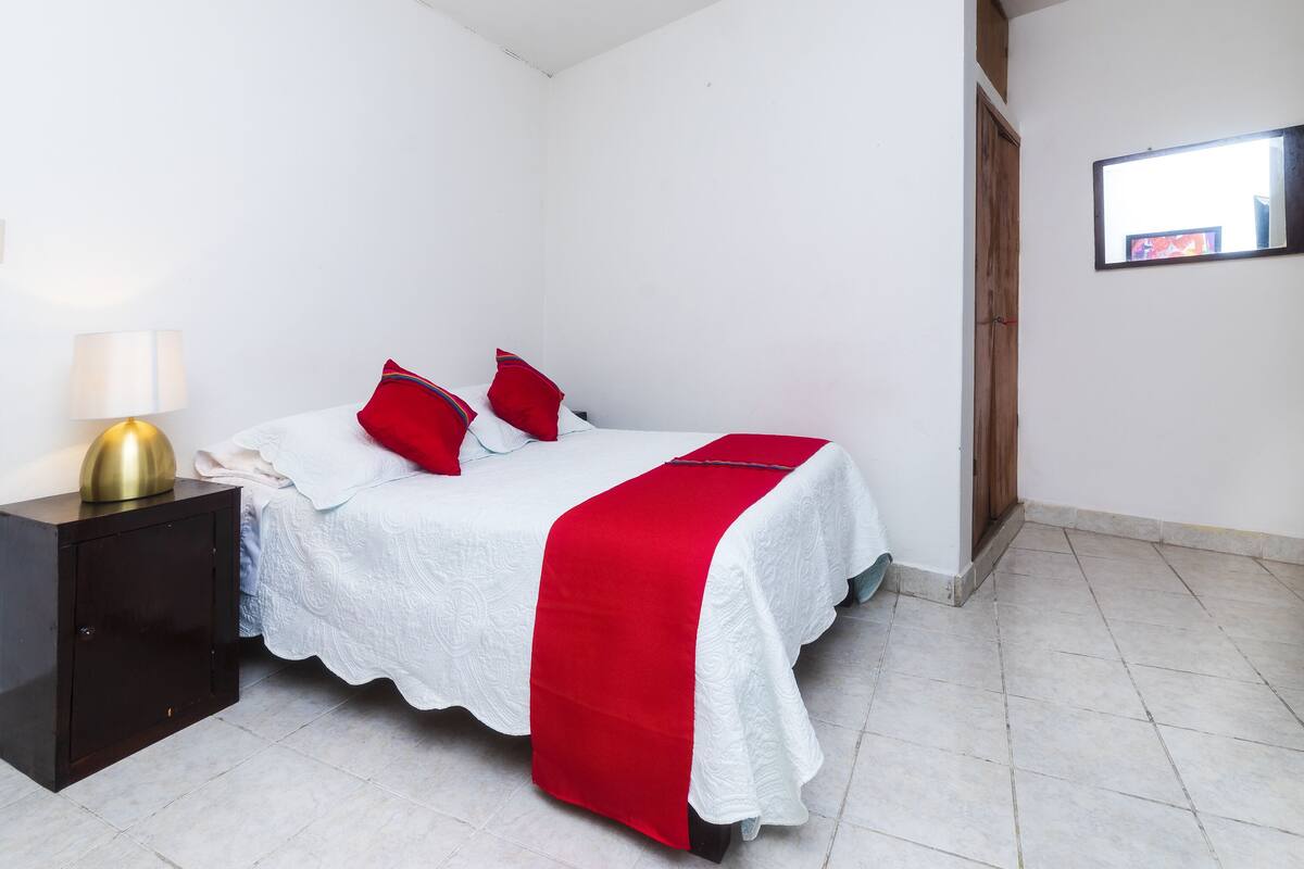 Ein Schlafzimmer mit einem Bett, einem Nachttisch, einer Lampe und einer roten und weißen Bettdecke.