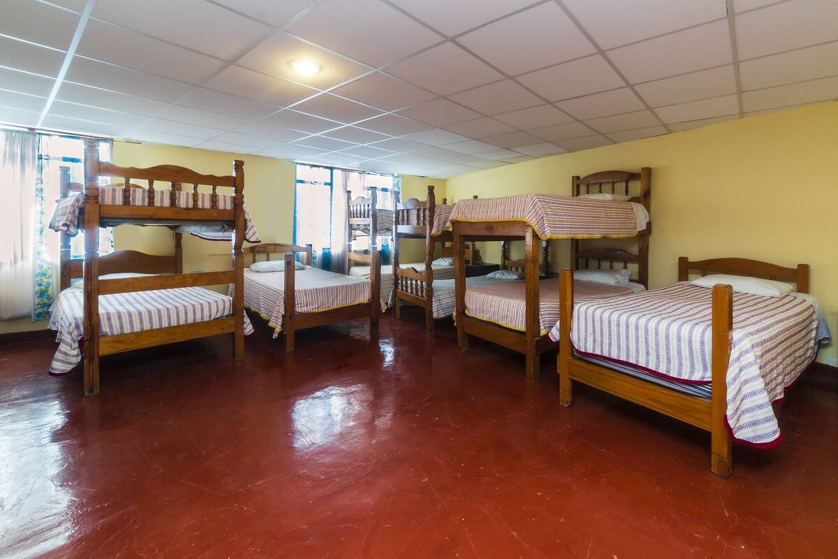 Ein Schlafsaalzimmer mit Etagenbetten, einer gefliesten Decke und einem Fenster mit Vorhängen.