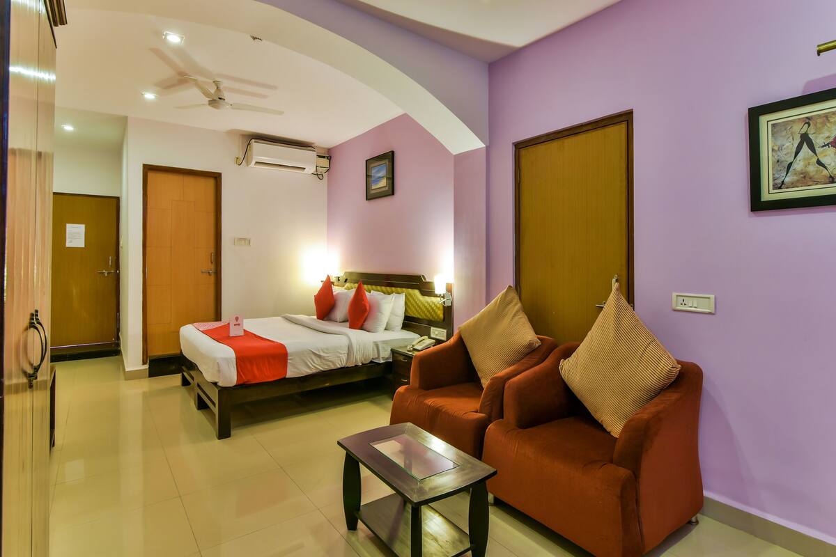 A hotel room with a bed, a sofa, a small table, and a ceiling fan.