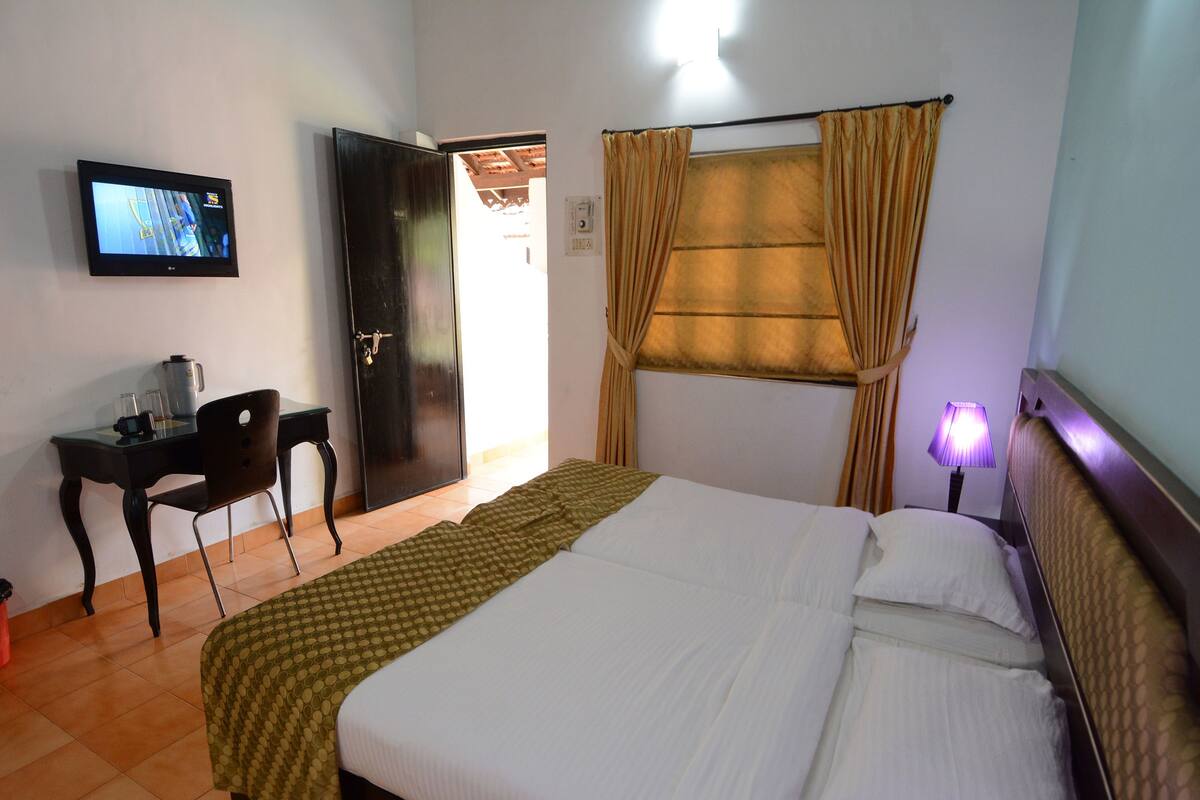 A hotel room with a bed, a desk with a chair, a television, and a window with curtains.