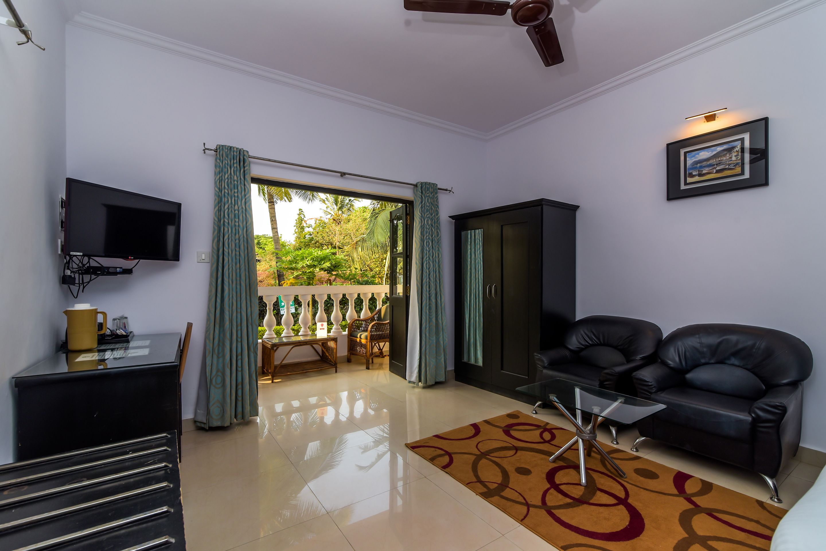 A living room with a TV, a sofa, a coffee table, and a view of a balcony with a railing and greenery.