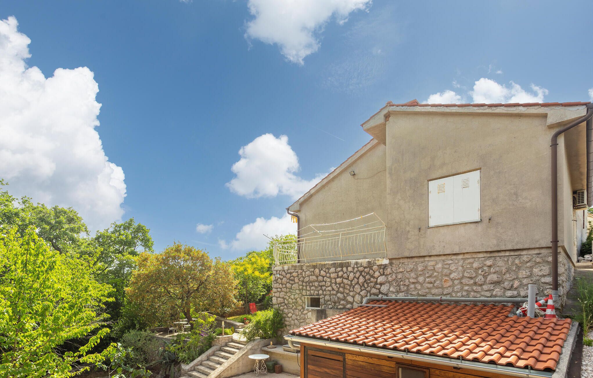 Un bâtiment avec une base en pierre et un toit recouvert de tuiles, entouré de verdure et sous un ciel dégagé.