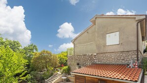 Un bâtiment avec une base en pierre et un toit recouvert de tuiles, entouré de verdure et sous un ciel dégagé.