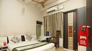 A hotel room with a bed, a desk, a chair, a mirror, an air conditioning unit, and a door with a 'Please do not disturb' sign. - OYO 1671 Hotel Sundaram (Prayagraj)