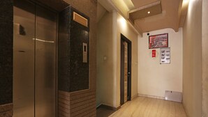 A hallway with marble flooring, two elevators, and a fire alarm panel on the wall. - OYO 1671 Hotel Sundaram (Prayagraj)