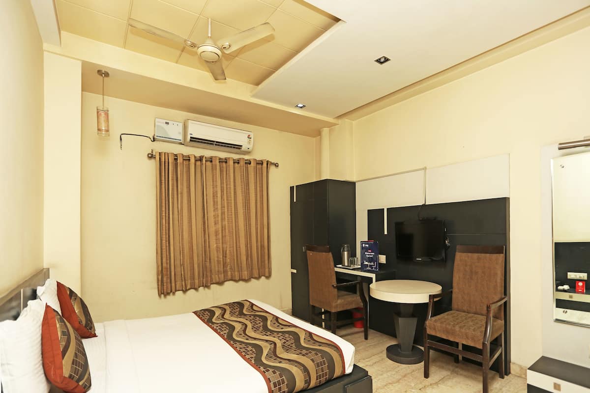 Habitación de hotel con cama, escritorio, dos sillas, televisor y aire acondicionado.