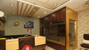 A reception area with a wooden reception desk, a mounted television, and a stone wall. - OYO 1671 Hotel Sundaram (Prayagraj)