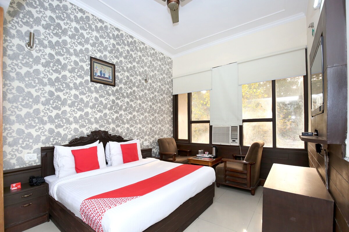 A hotel room with a large bed, a desk with a chair, a TV, and a window with blinds.
