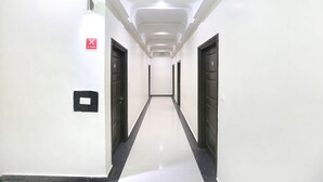A long, narrow hallway with white walls and a shiny floor, leading to a door at the end. - Capital O 9235 Hotel Nayyar (Amritsar)