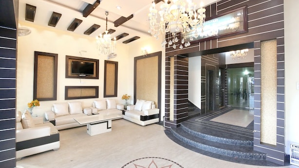 A modern living room with a sectional sofa, a flat-screen TV, and a chandelier. - Capital O 9235 Hotel Nayyar (Amritsar)