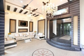 A modern living room with a sectional sofa, a flat-screen TV, and a chandelier. - Capital O 9235 Hotel Nayyar (Amritsar)
