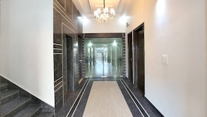 A modern hotel lobby with a marble staircase, a chandelier, and a glass door leading to the reception area. - Capital O 9235 Hotel Nayyar (Amritsar)