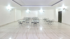 A spacious conference room with a polished marble floor, multiple tables and chairs, and recessed ceiling lighting. - Capital O 9235 Hotel Nayyar (Amritsar)