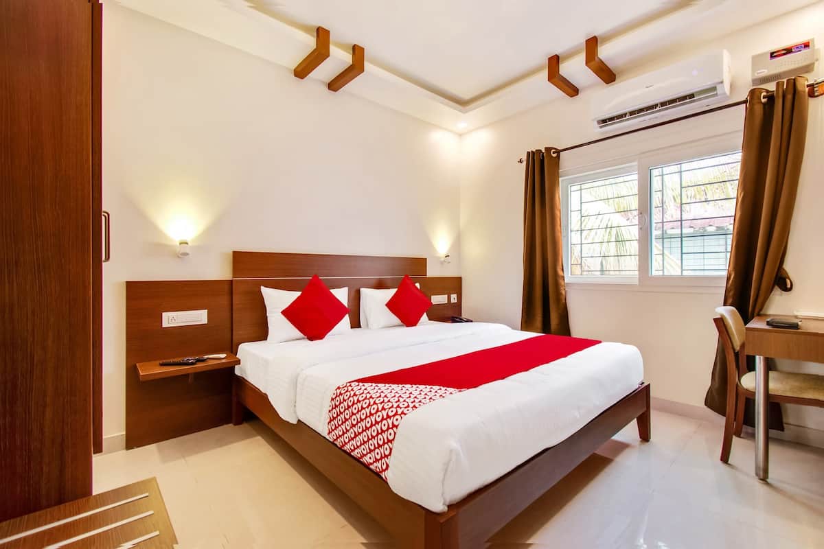 A hotel room with a wooden bed, red pillows, a desk, and a window with curtains.