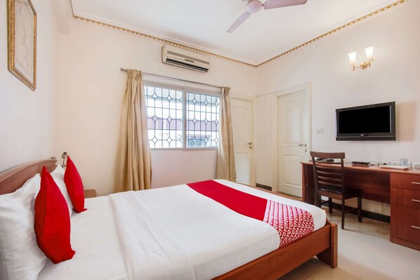 A hotel room with a bed, a desk, a chair, a television, and an air conditioning unit.
