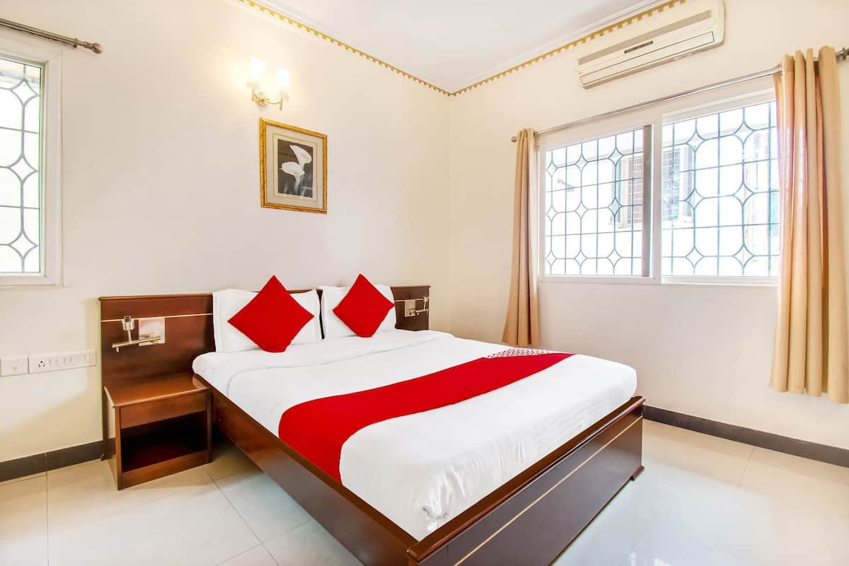 A hotel room with a large bed, a nightstand, a wall-mounted air conditioner, and a window with curtains.
