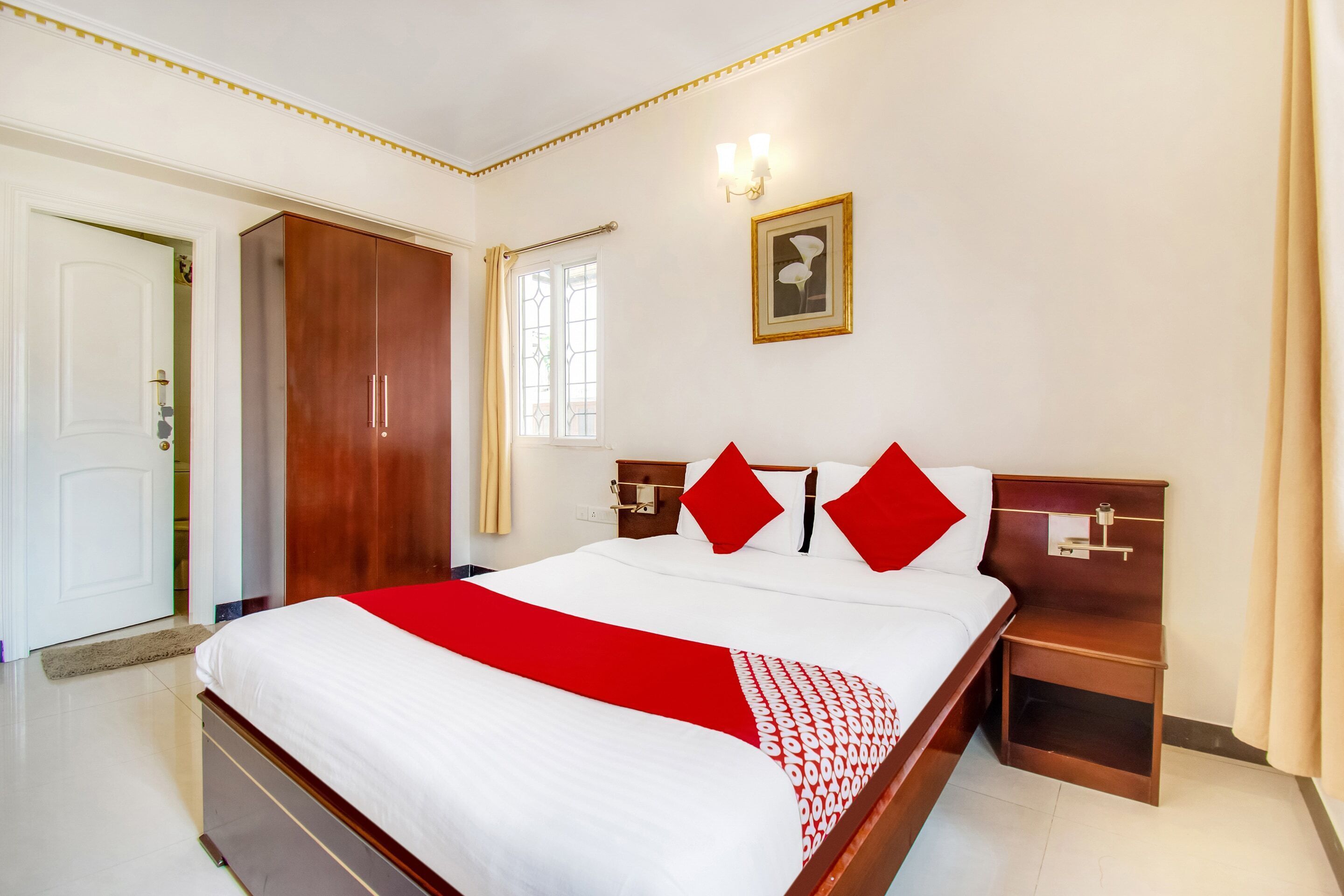 A hotel room with a large bed, wooden headboard, two bedside tables, a wardrobe, and a framed picture on the wall.