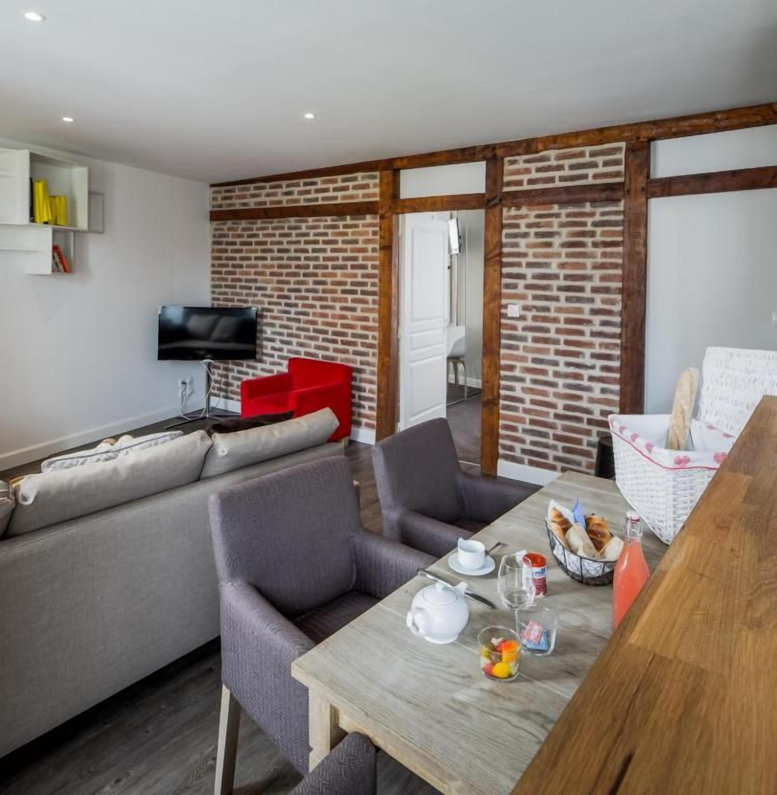 A modern living space with a sofa, chairs, a dining table with breakfast items, a TV, and a brick wall.
