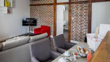 A modern living space with a sofa, chairs, a dining table with breakfast items, a TV, and a brick wall.