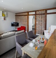 Un espacio moderno para vivir con sofá, sillas, una mesa de comedor con alimentos para el desayuno, televisión y una pared de ladrillo.