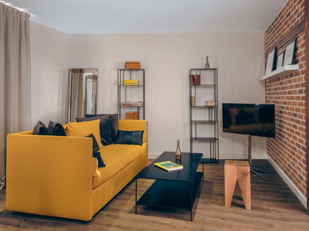 A living room with a yellow sofa, a black coffee table, a TV, and two shelves with books and decorative items.
