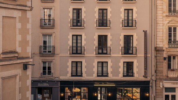 Un hotel de diverses plantes amb un estil arquitectònic europeu clàssic, que destaca per balcons uniformes i una entrada central amb portes de vidre.