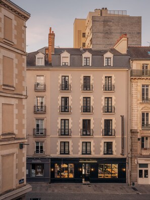 Un hotel de varios pisos con un estilo arquitectónico europeo clásico, que cuenta con balcones uniformes y una entrada central con puertas de cristal.