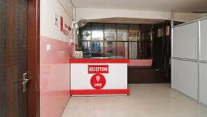 A reception desk with a 'RECEPTION' sign and an 'OYO' logo, a door to the left, and a window with curtains. - OYO 4979 Prabha Palace Lodge (Guwahati)