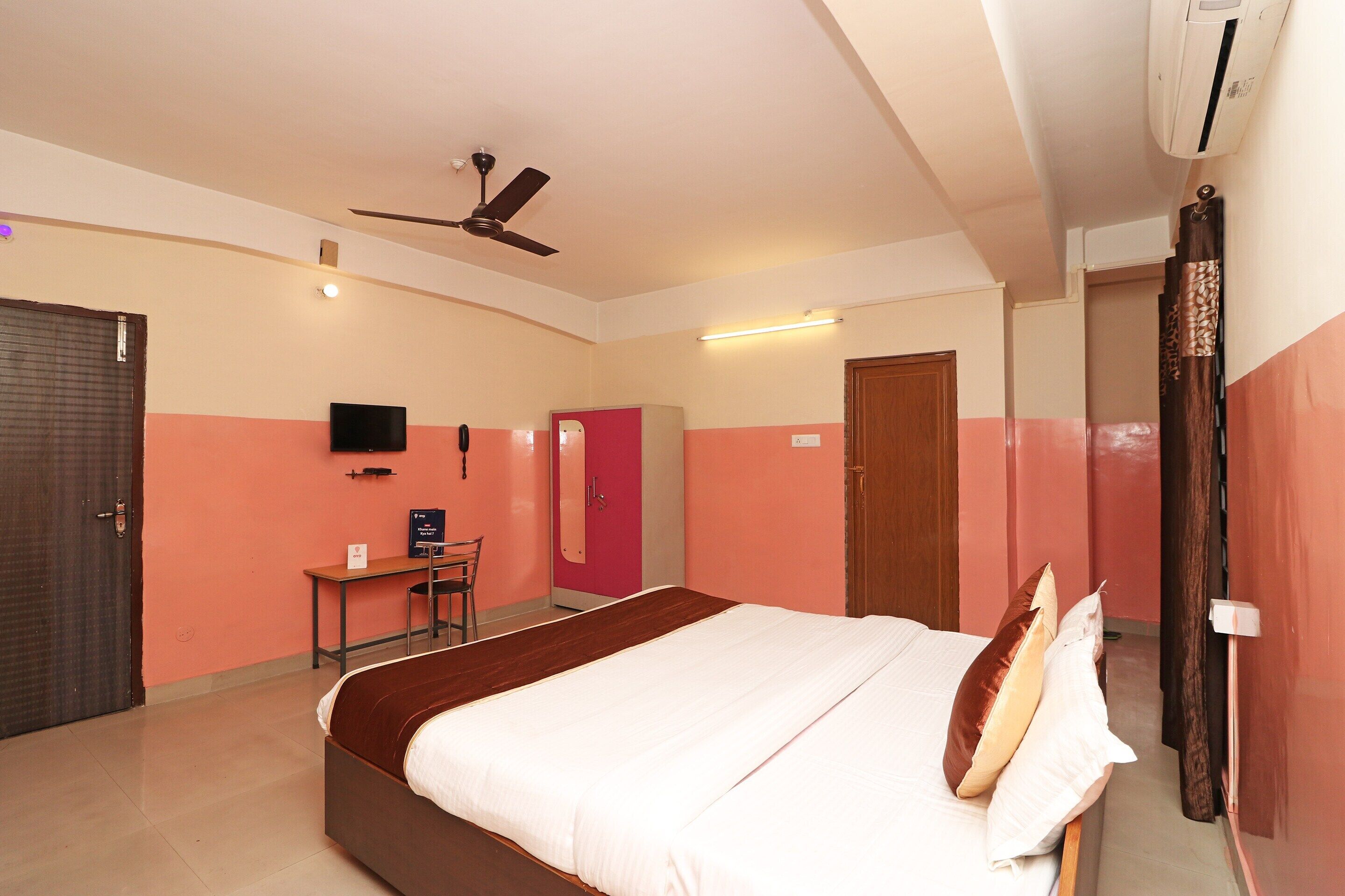 A hotel room with a bed, a desk, a chair, a television, and a ceiling fan.