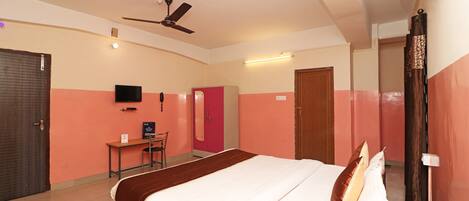 A hotel room with a bed, a desk, a chair, a television, and a ceiling fan.