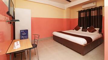 Habitación de hotel con cama, escritorio, silla, televisor montado en la pared y equipo de aire acondicionado.